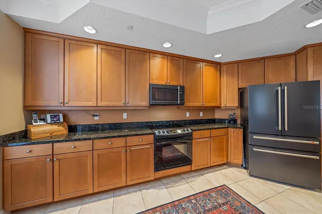 a kitchen with granite countertop stainless steel appliances a sink dishwasher a stove top oven a refrigerator with wooden cabinets and floor