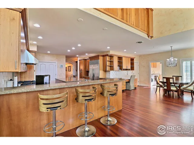 a kitchen with stainless steel appliances granite countertop a refrigerator a stove a sink a dining table and chairs with wooden floor