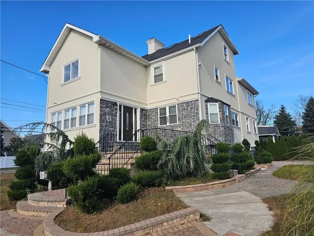 a view of a white building among the street with plants and trees