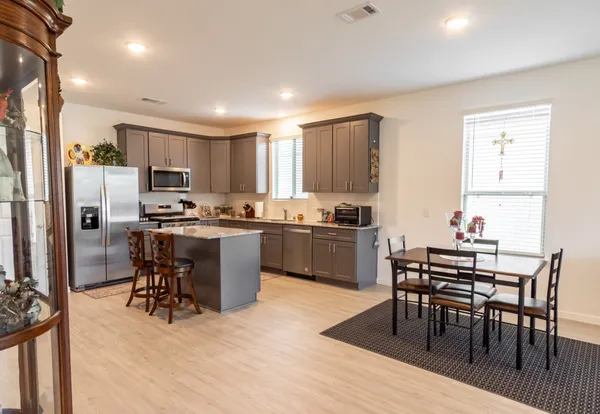 a kitchen with stainless steel appliances granite countertop a dining table chairs refrigerator and sink
