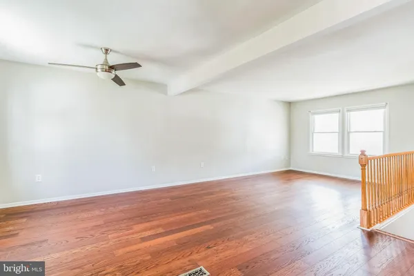 an empty room with wooden floor ceiling fan and windows