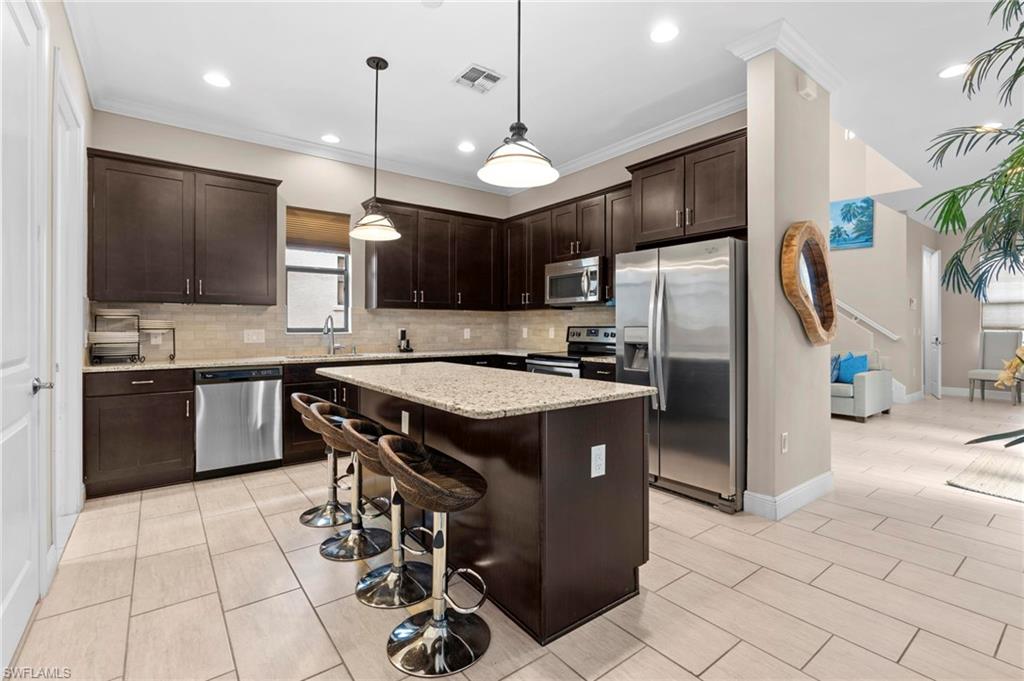 1300 Kendari Terrace Naples, FL 34113 - Photo 9 of 31 a kitchen with stainless steel appliances granite countertop a stove a refrigerator a sink a oven with a dining table and chairs