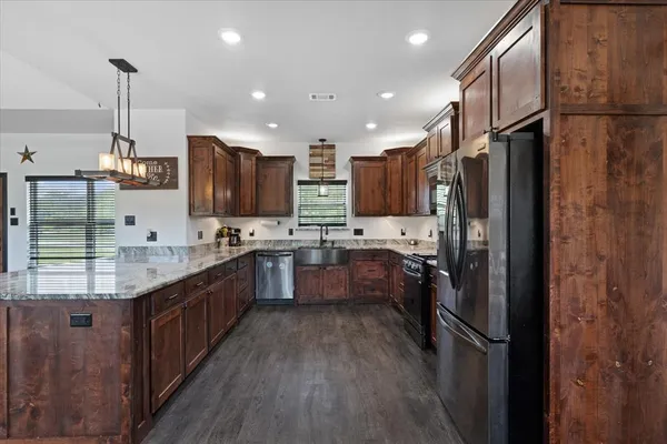 a kitchen with stainless steel appliances granite countertop a refrigerator a sink dishwasher a oven and a dining table with wooden floor