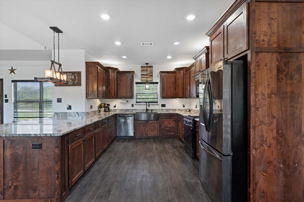 403 Polk Road Bowie, TX 76230 - Photo 8 of 36 Kitchen featuring appliances with stainless steel finishes, a peninsula, dark wood-type flooring, light stone counters, and dark brown cabinets