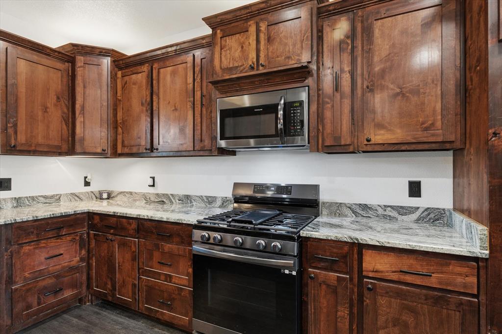 403 Polk Road Bowie, TX 76230 - Photo 9 of 36 Kitchen with stainless steel appliances, light stone counters, and dark wood-style flooring