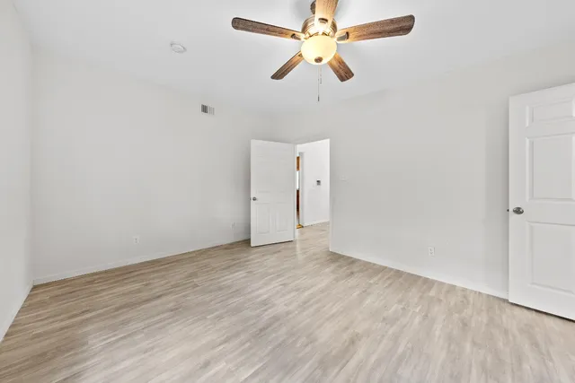 an empty room with wooden floor ceiling fan and window