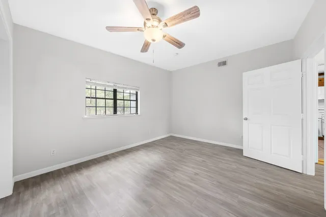 an empty room with wooden floor ceiling fan and windows