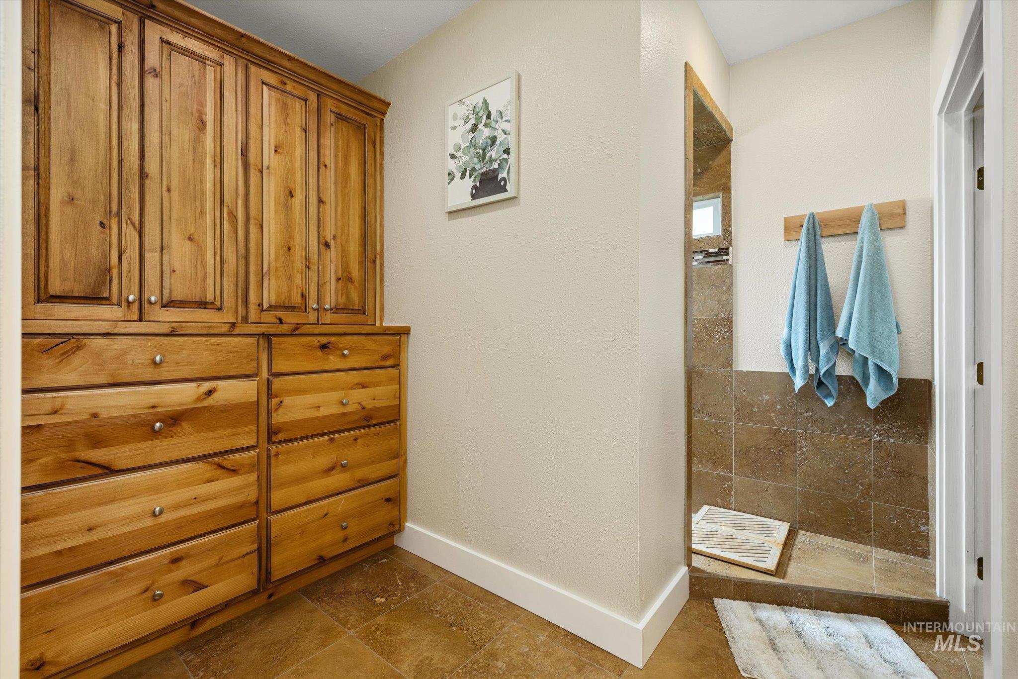 1140 Edgemont Road Emmett, ID 83617 - Photo 18 of 50 Built-in wood cabinetry with chrome hardware, full-height shower with stone-look tile surround, recessed shower niche, and coordinating stone-look floor tile