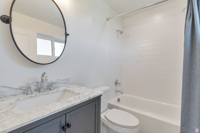 1820 West Farmhouse Flats Road Peoa, UT 84061 - Photo 34 of 79 Bathroom featuring a dark grey vanity with a white countertop and undermount sink, a round black framed mirror, a white toilet, and a white tiled shower-over-tub combination with chrome fixtures