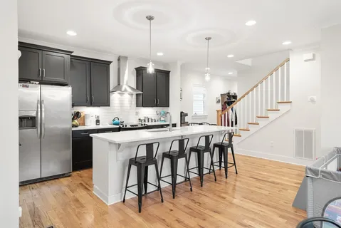a kitchen with stainless steel appliances kitchen island granite countertop a refrigerator a stove a kitchen island with wooden floor cabinets and chairs