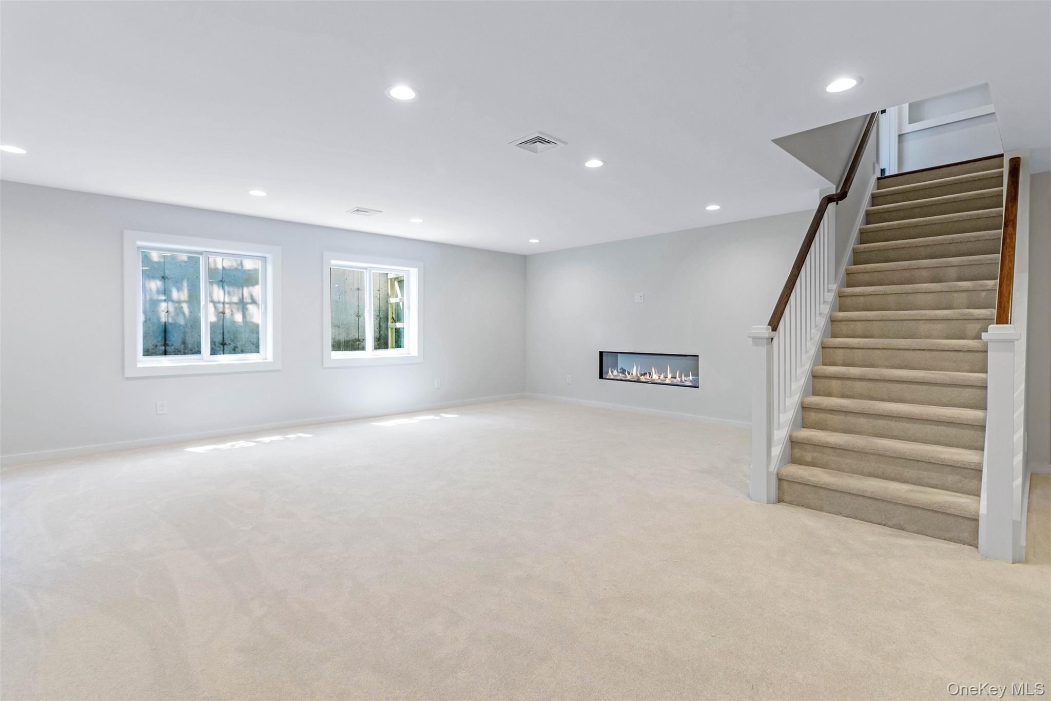 130 Sunset Lane Greenport, NY 11944 - Photo 22 of 34 Unfurnished living room with a glass covered fireplace, recessed lighting, light colored carpet, and stairs