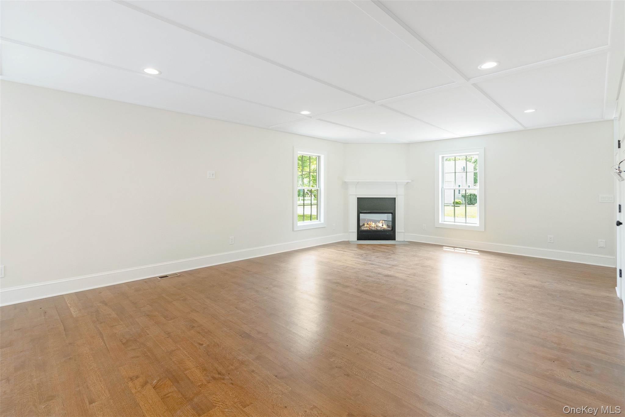 130 Sunset Lane Greenport, NY 11944 - Photo 8 of 34 Unfurnished living room featuring plenty of natural light, wood finished floors, a glass covered fireplace, recessed lighting, and coffered ceiling