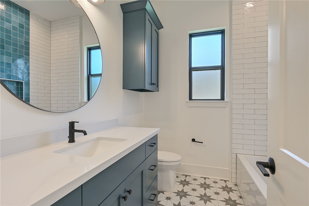 5115 Inverness Drive Bryan, TX 77802 - Photo 17 of 28 Bathroom featuring shower/tub combo, Vanity with integrated sink and matte black faucet, featuring a large round mirror, upper cabinetry, and patterned floor tiling
