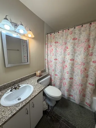a bathroom with a granite countertop sink toilet a mirror and shower curtain