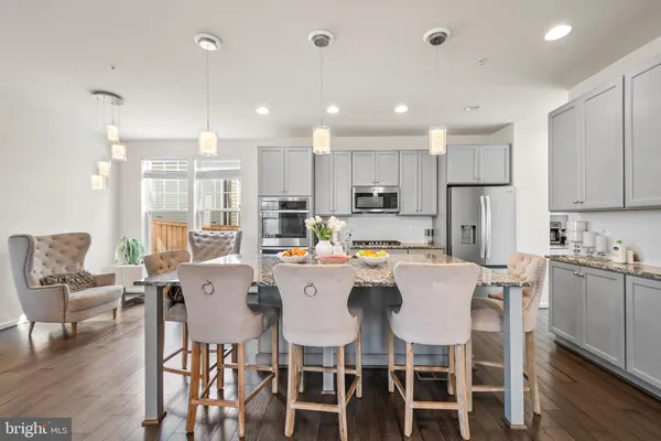a kitchen with stainless steel appliances kitchen island granite countertop a dining table chairs refrigerator and sink