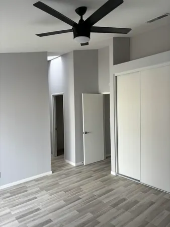 a view of an empty room with wooden floor and a ceiling fan