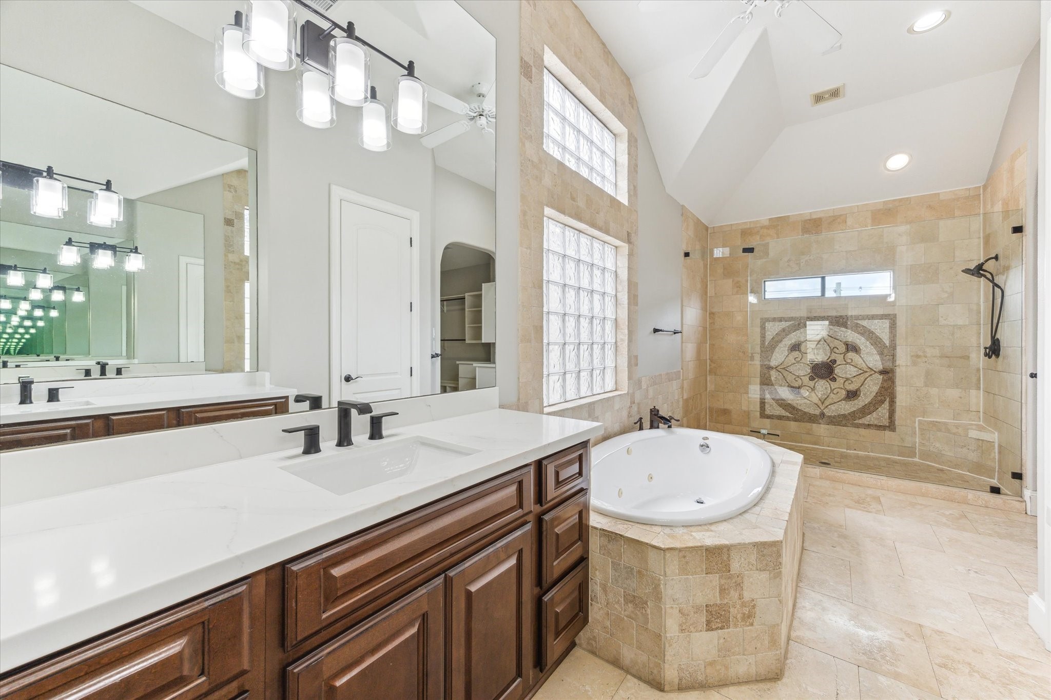 1512 Thompson Street, Unit 3 Houston, TX 77007 - Photo 9 of 32 This bathroom features a spacious layout with a luxurious whirlpool tub, large walk-in shower with intricate tile design, and dual sinks with modern fixtures. The room is accented with ample natural light from glass block windows and sleek lighting fixtures.