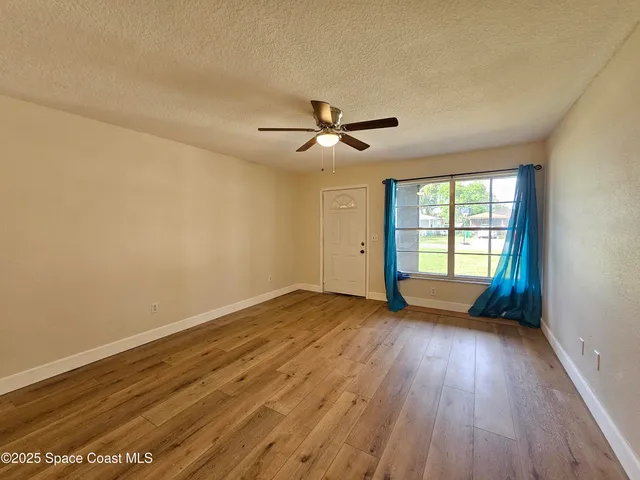 a view of empty room with wooden floor and fan