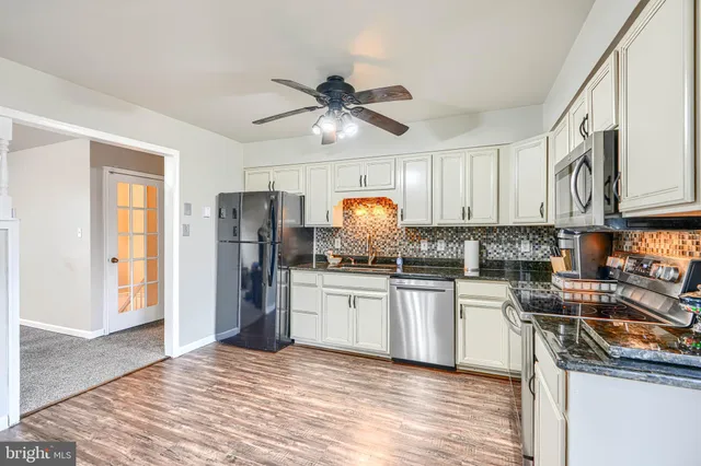 a kitchen with granite countertop a refrigerator a sink and white cabinets