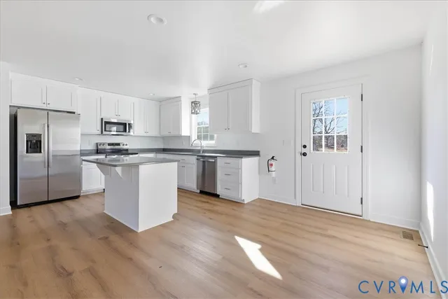 a kitchen with stainless steel appliances granite countertop a stove a sink dishwasher a refrigerator and white cabinets with wooden floor