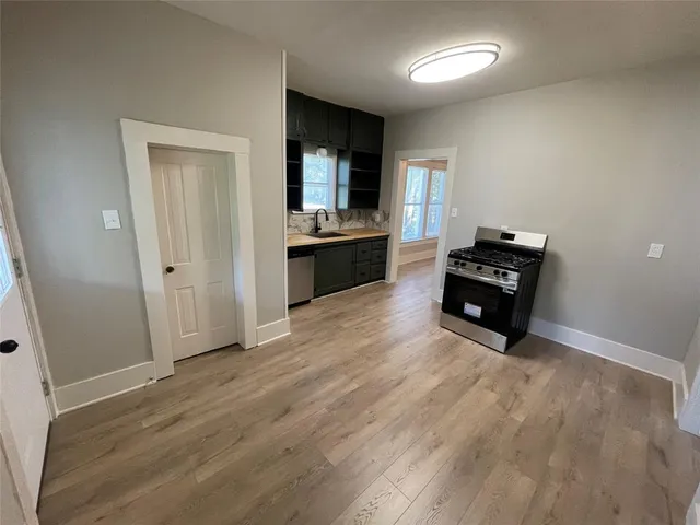 an empty room with wooden floor and kitchen view
