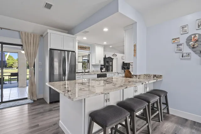 a kitchen with stainless steel appliances granite countertop a dining table chairs refrigerator and sink