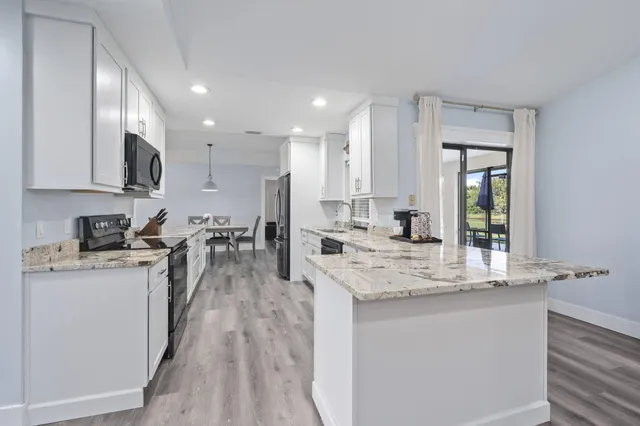 a kitchen with stainless steel appliances granite countertop a stove top oven a sink dishwasher and a refrigerator with wooden floor