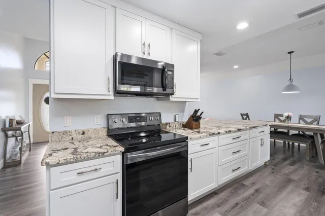 a kitchen with stainless steel appliances granite countertop a sink dishwasher stove and white cabinets with wooden floor