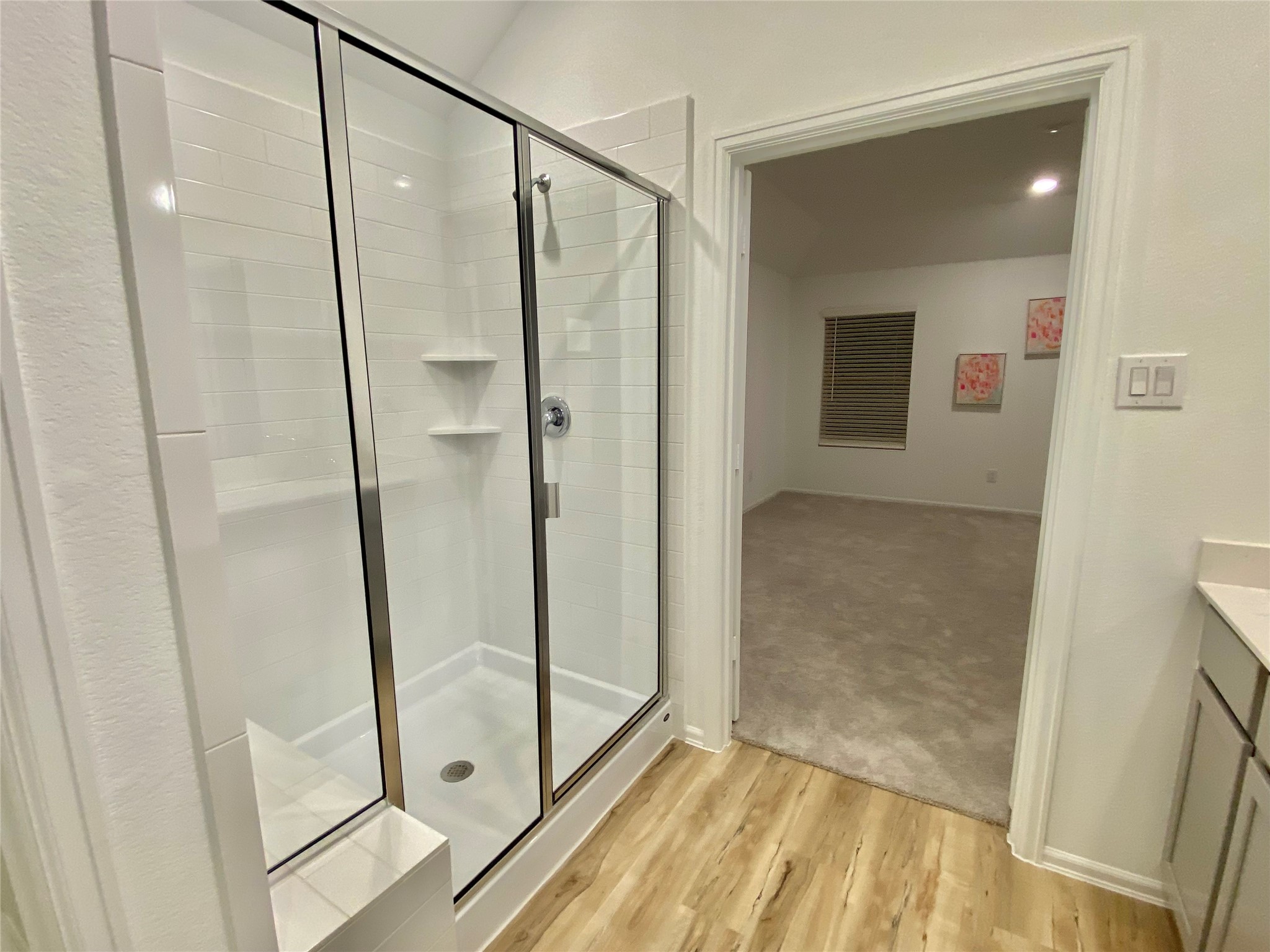 3724 Moss Hl Road Rosenberg, TX 77469 - Photo 16 of 29 This photo showcases a modern bathroom with a glass-enclosed shower and sleek white tiles, opening into a carpeted room with soft lighting.