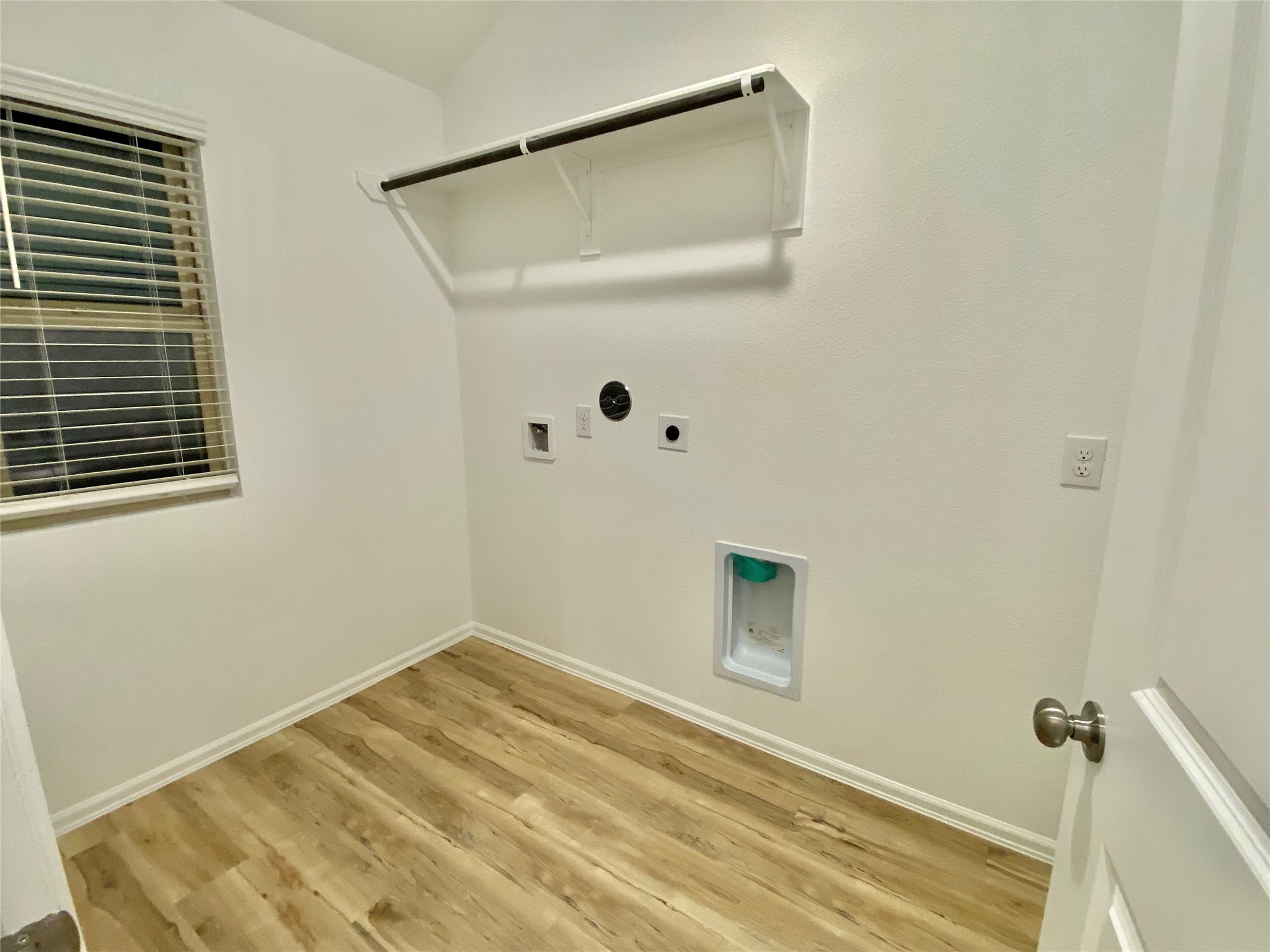 3724 Moss Hl Road Rosenberg, TX 77469 - Photo 17 of 29 A bright laundry room with hardwood floors, white walls, and a window for natural light. It features hookups for a washer and dryer, an overhead shelf, and a hanging rod for convenience.