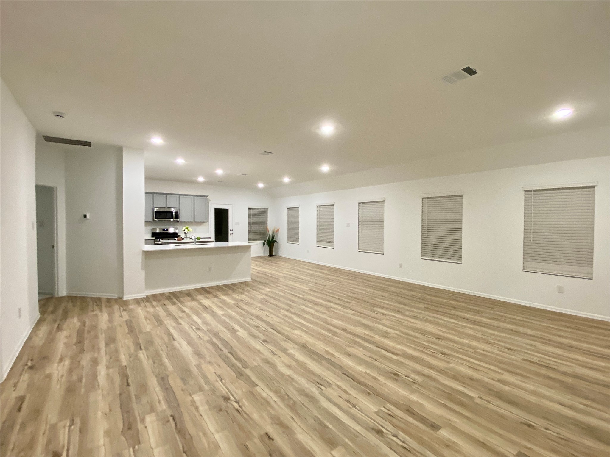 3724 Moss Hl Road Rosenberg, TX 77469 - Photo 4 of 29 This photo showcases a spacious, open-plan living area with light wood flooring and neutral walls. The modern kitchen features stainless steel appliances and a large countertop, perfect for entertaining. Multiple windows provide natural light, creating a bright and inviting atmosphere.