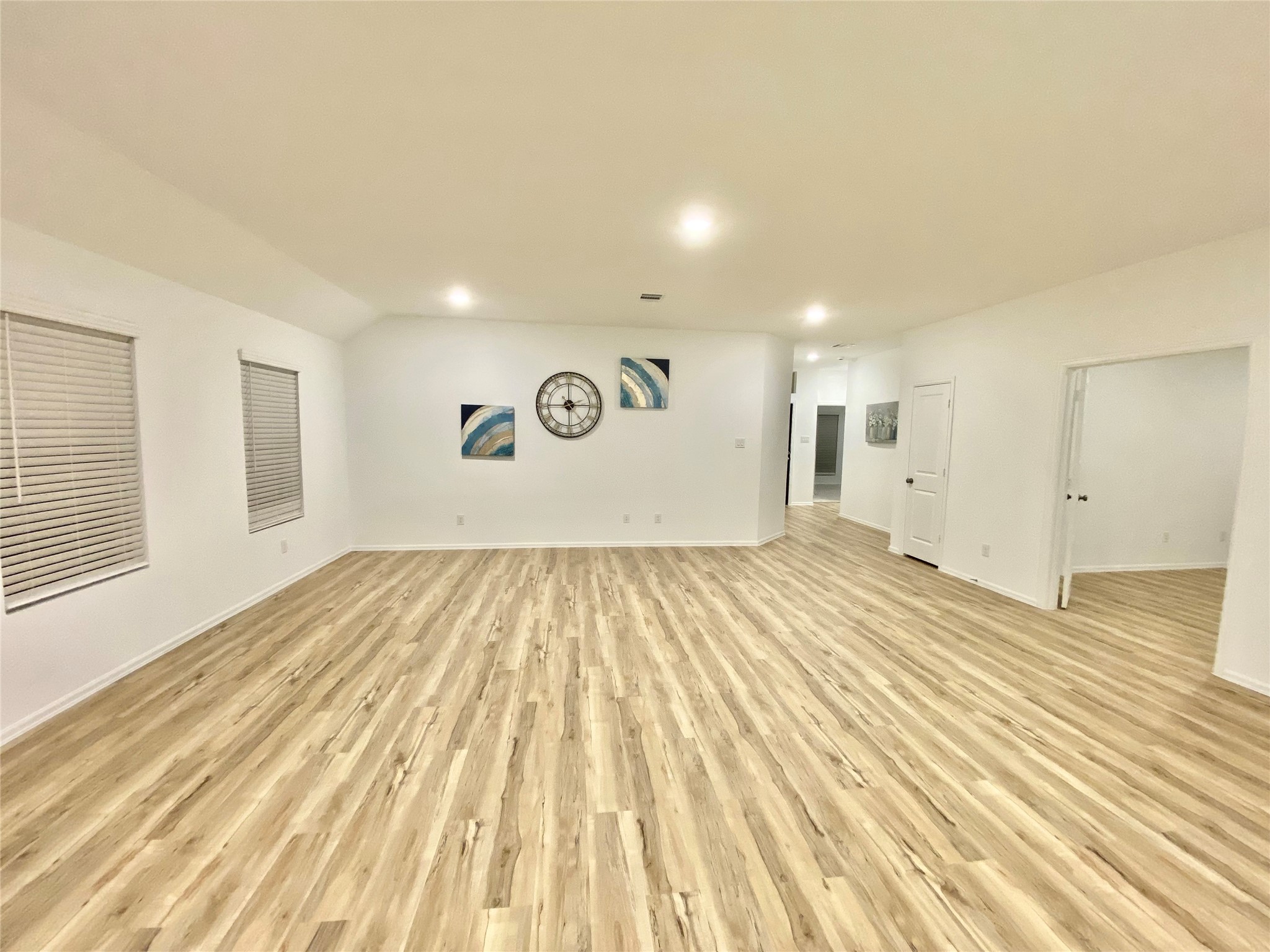 3724 Moss Hl Road Rosenberg, TX 77469 - Photo 7 of 29 Spacious and bright living area with light wood flooring, white walls, and recessed lighting. Features modern decor, including abstract art and a large wall clock. Multiple doorways provide access to adjoining rooms.