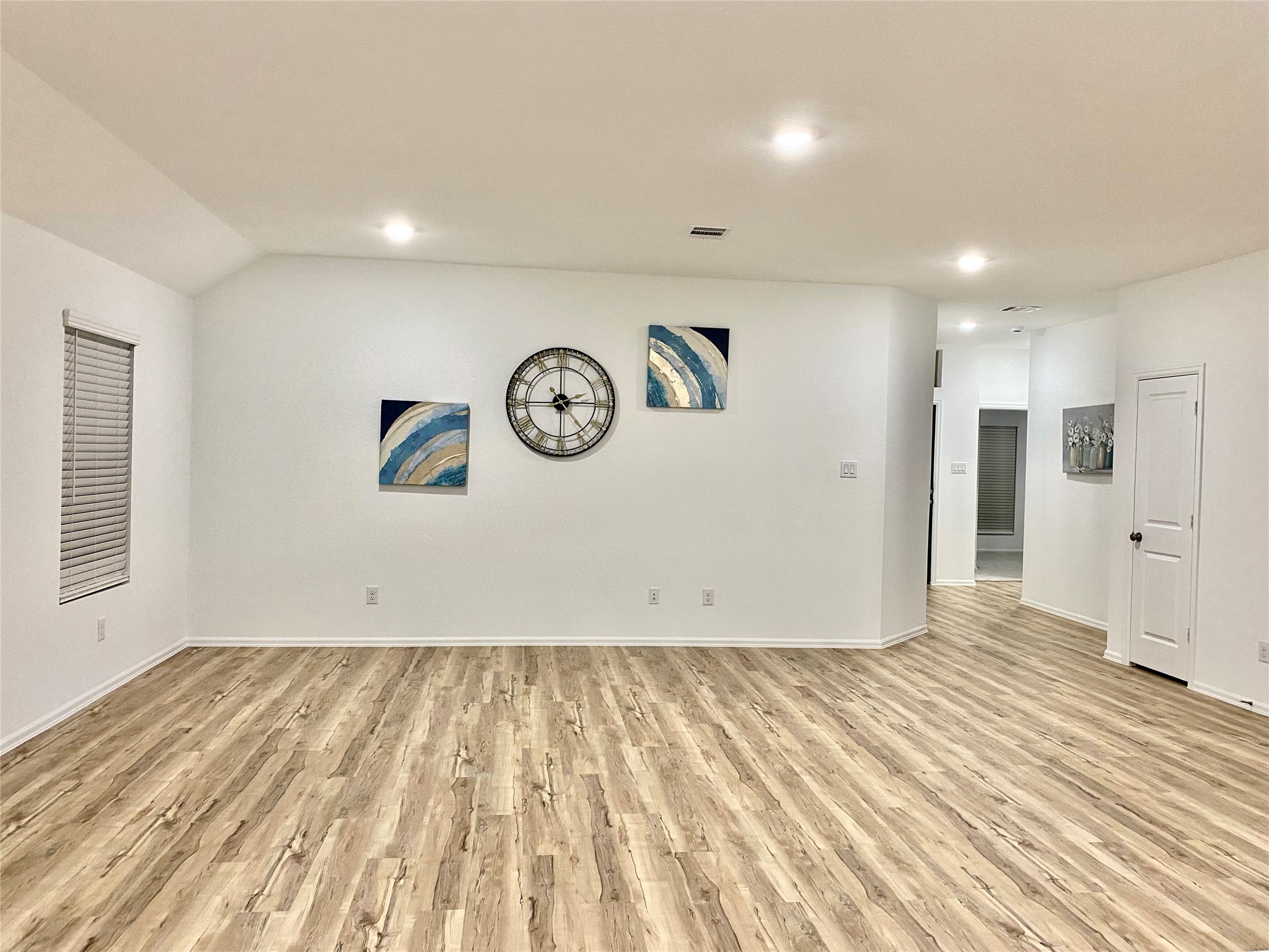 3724 Moss Hl Road Rosenberg, TX 77469 - Photo 8 of 29 This photo showcases a spacious, well-lit living area with light wood flooring and minimalist decor. It features recessed lighting, a large wall clock, and modern artwork, creating a clean and inviting atmosphere.