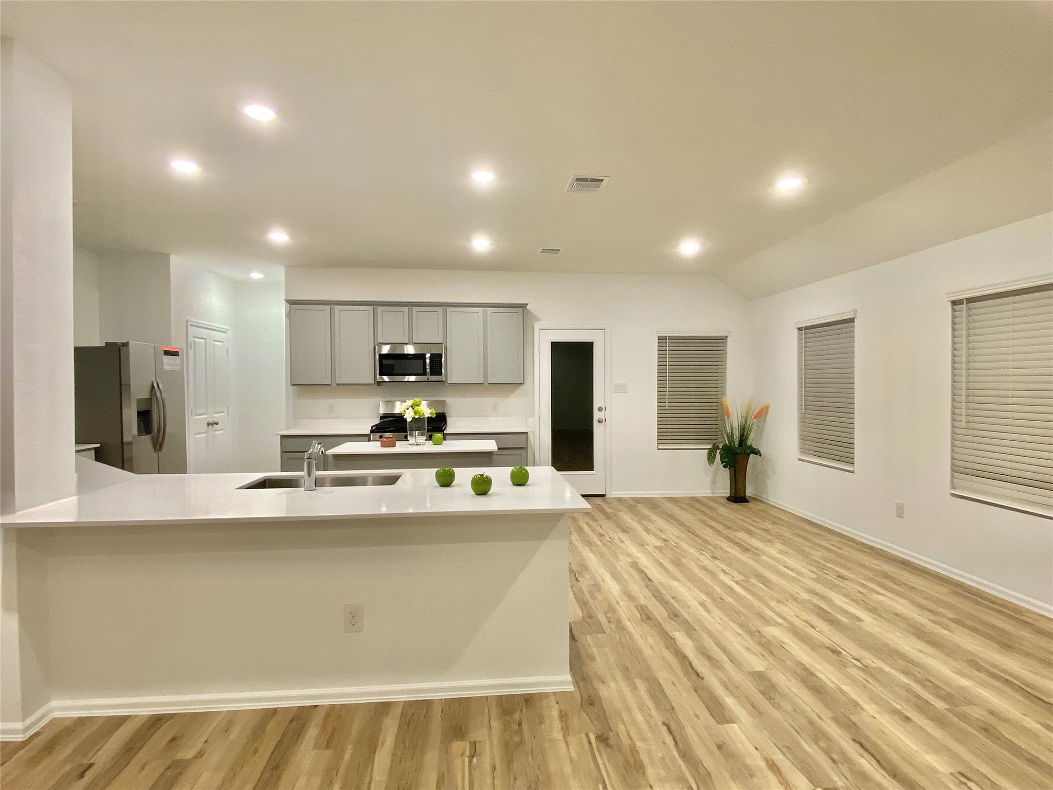 3724 Moss Hl Road Rosenberg, TX 77469 - Photo 10 of 29 This photo features a modern, open-concept kitchen and living area with sleek light fixtures. The kitchen has stainless steel appliances, a large island with a sink, and neutral cabinetry. The space is bright with light wood flooring and ample windows.