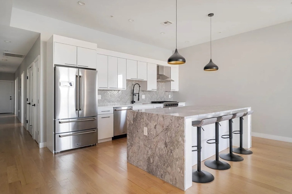 243 Condor Street, Unit 4 Boston, MA 02128 - Photo 5 of 13 a kitchen with kitchen island a counter top space wooden floor and stainless steel appliances