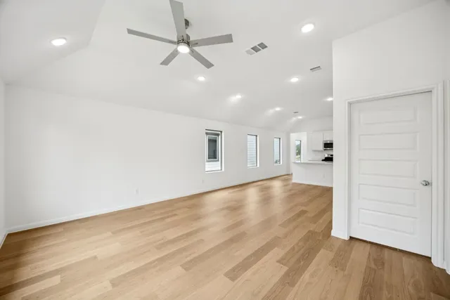 an empty room with wooden floor ceiling fan and windows
