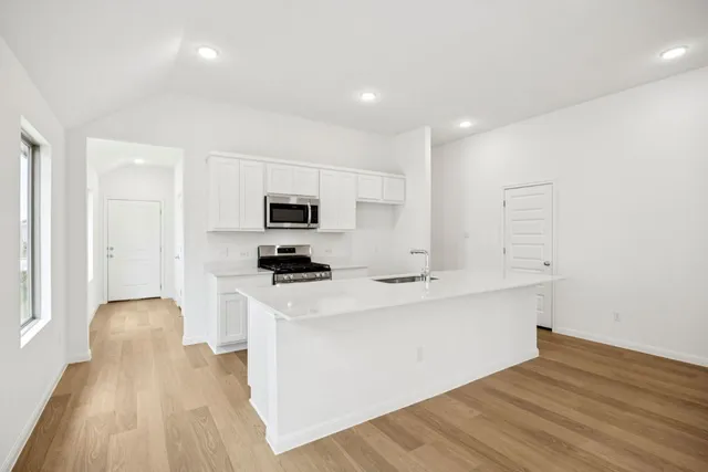 a kitchen with stainless steel appliances a sink a stove a microwave a refrigerator a white cabinets and wooden floor