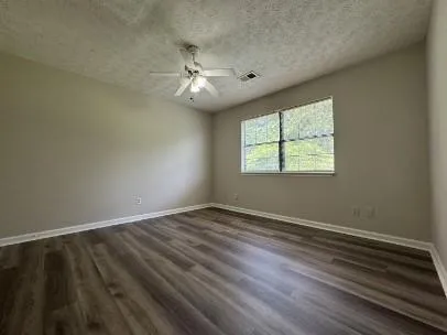 an empty room with wooden floor fan and windows