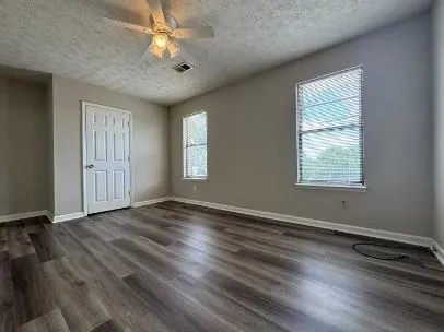 an empty room with wooden floor chandelier fan and windows