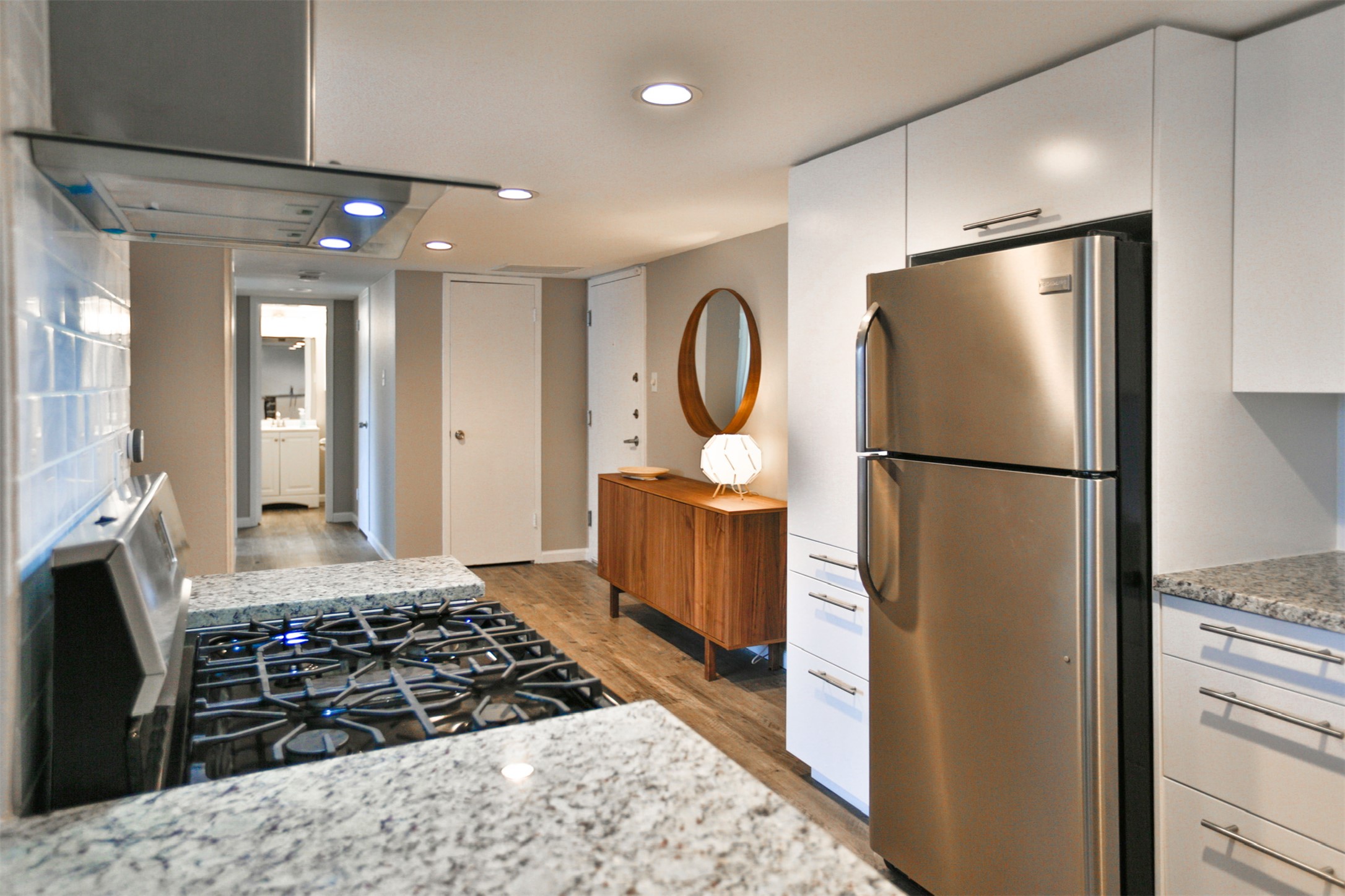1800 Lavaca Street, Unit A608 Austin, TX 78701 - Photo 4 of 12 Kitchen with stainless steel appliances, white cabinets, light stone counters, ventilation hood, and light wood-style flooring