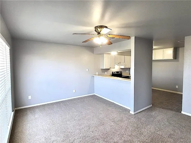 an empty room with a kitchen and a ceiling fan