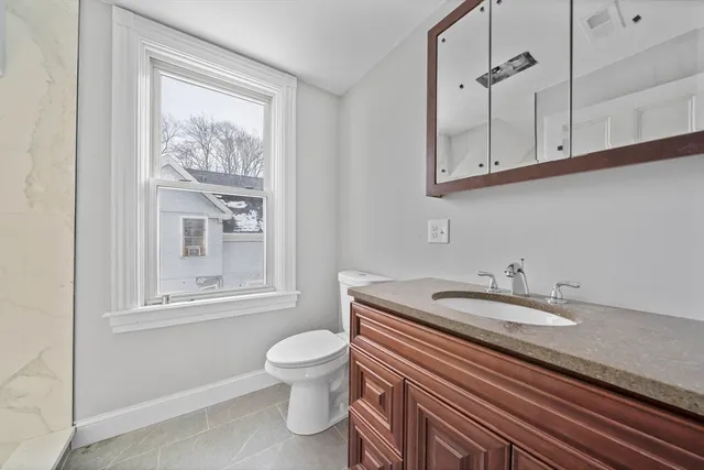 a bathroom with a granite countertop sink a toilet and a window