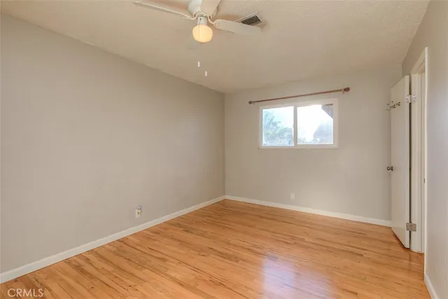 an empty room with wooden floor fan and windows