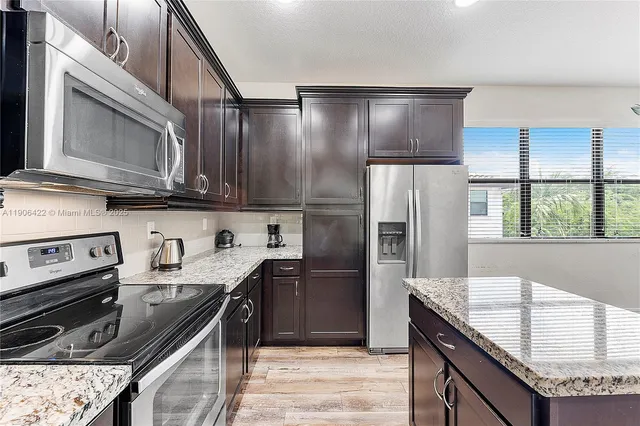 a kitchen with stainless steel appliances granite countertop a refrigerator a stove and a sink with wooden cabinets
