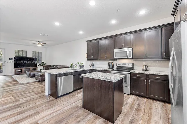 a kitchen with stainless steel appliances granite countertop a stove top oven a sink dishwasher a refrigerator and a microwave oven with wooden floor