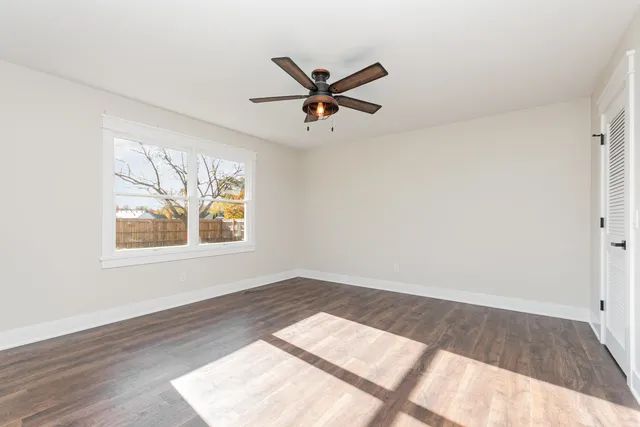 an empty room with wooden floor chandelier fan and windows