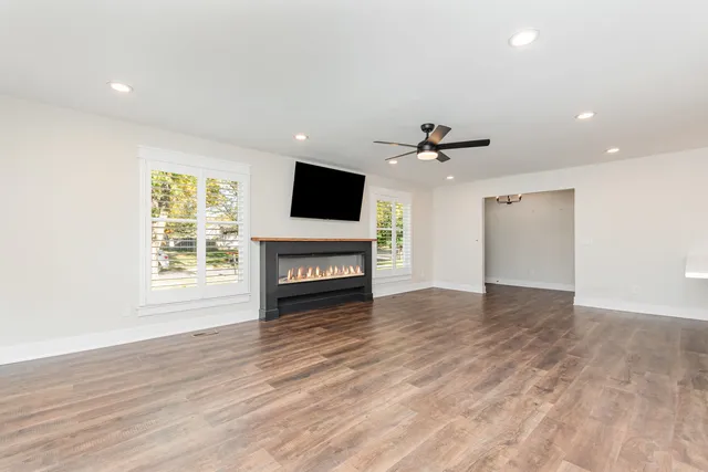 a view of a livingroom with a fireplace a ceiling fan and wooden floor