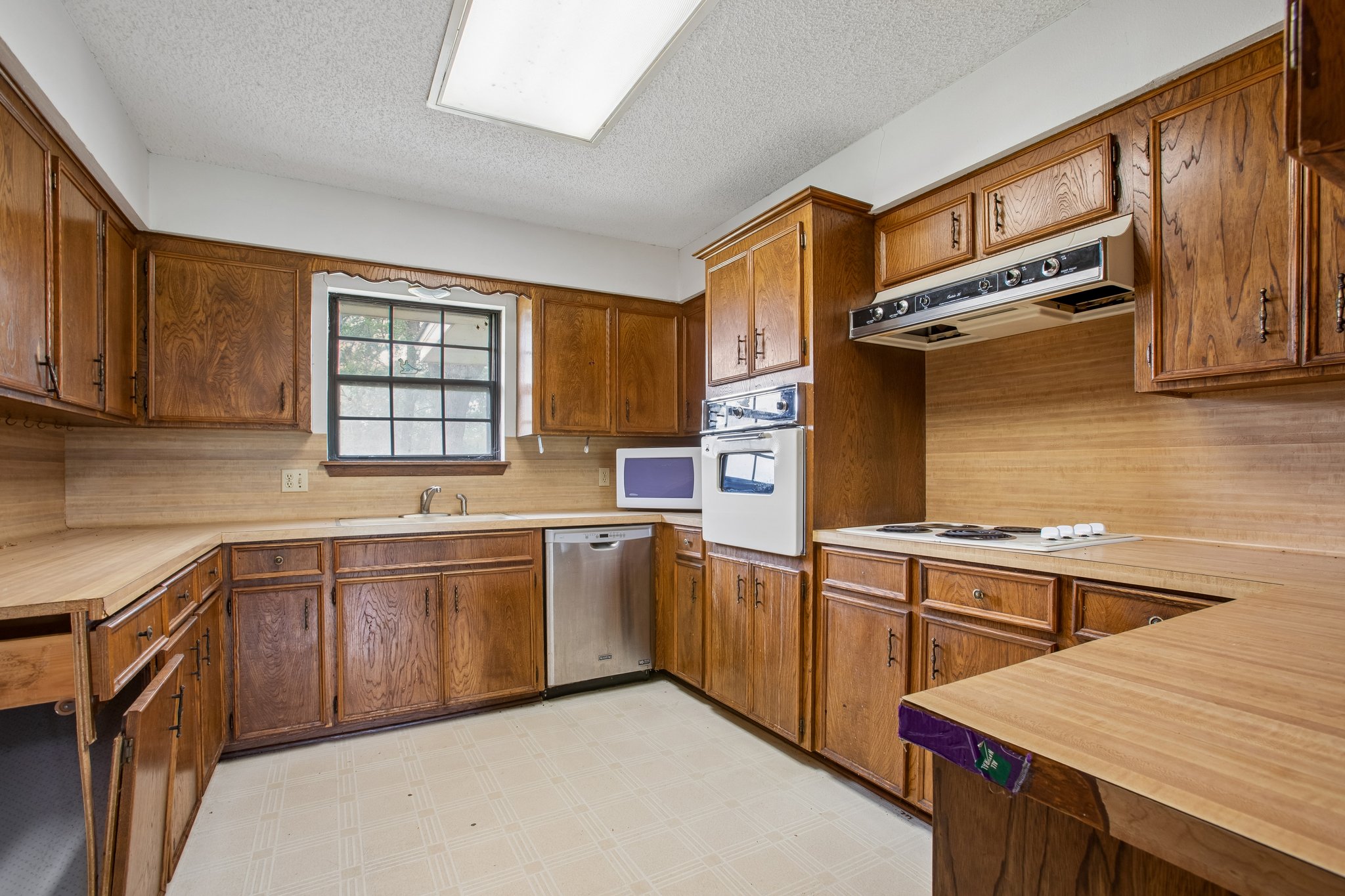 406 Monkey Road Elgin, TX 78621 - Photo 10 of 39 Kitchen featuring wood-finish cabinetry, light-toned countertops, a stainless steel dishwasher, an integrated wall oven, and a built-in cooktop with an overhead range hood