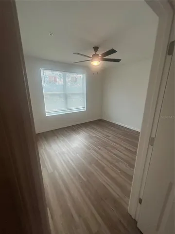 an empty room with wooden floor fan and windows