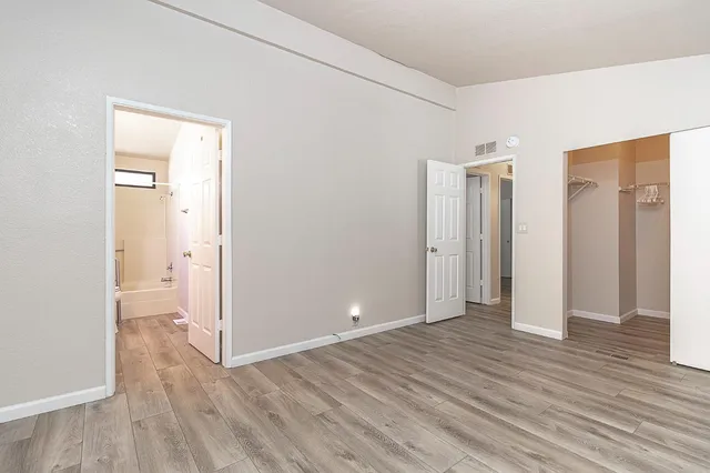 a view of an empty room with wooden floor and a bathroom